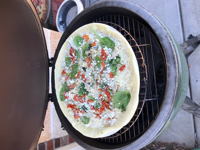 Big green egg open with uncooked pizza